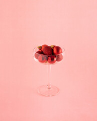 Red Christmas decorative baubles in the champagne glass against pastel pink background. Minimal celebration concept. Party time. 