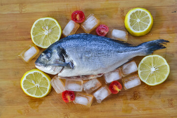 fresh fish sea ​​bream with lemon on the wooden table with lemon spices and cherry tomato
