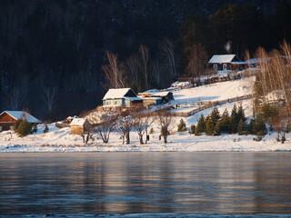 
Family in the village during the Christmas holidays.  Russian  rustic wooden houses with smoke from chimneys about of the river. In background are forested mountains In the snow. Winter landscape.