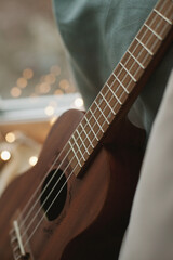 Fototapeta premium Ukulele on the windowsill with cozy pillows and lights at home closeup