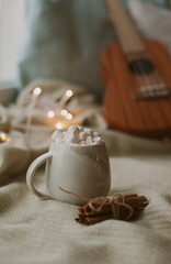 Hot cocoa with marshmallows and cinnamon sticks with christmas lights and guitar at night