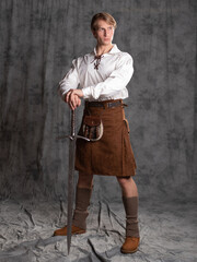A young man in a leather kilt and a white lace-up blouse. A Scottish knight with a two-handed...