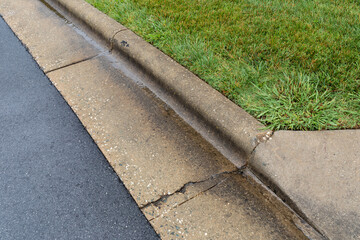 Close view of water draining alongside a concrete curb separating green grass from wet asphalt road surface, horizontal aspect - obrazy, fototapety, plakaty