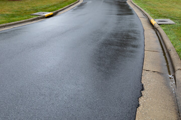 Sweeping asphalt roadway wet from rain, water draining on each side between the curbs to storm...