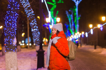 Obraz premium Girl having fun on christmas decoration lights street. Young happy smiling woman wearing stylish knitted scarf and jacket outdoors. Model laughing. Winter wonderland city scene, New Year party.