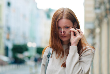 Portrait of a woman in the street. Glasses on his face. Red hair.