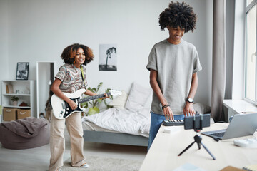 Portrait of two African-American young people playing music at home and recording video or livestream, copy space