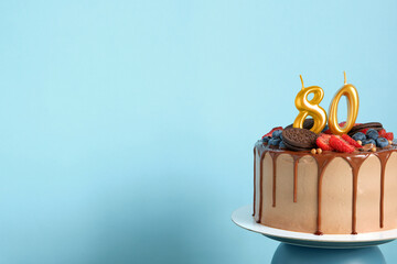 Chocolate birthday cake with berries, cookies and number eighty golden candles on blue wall...