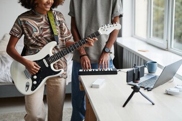 Cropped portrait of young African-American woman playing guitar at home and recording video or...