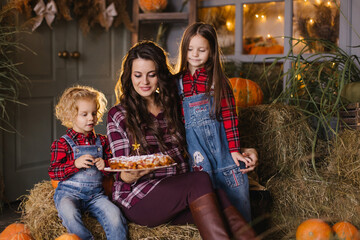 Mother with children eating apple pie. Celebrating Thanksgiving on the veranda of a country house. Mom and two daughters in plaid shirts. Delicious homemade baked goods. DIY baked pie. Siblings
