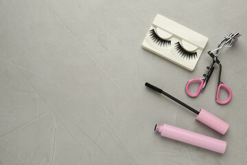 False eyelashes, curler and mascara on grey table, flat lay. Space for text