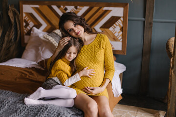 Obraz na płótnie Canvas Child hugs mom's pregnant belly. Happy parenting. Expectation of the second child. The sister is waiting for her brother. Siblings. Eco parenting. Cozy boho country interior. Mothers Day