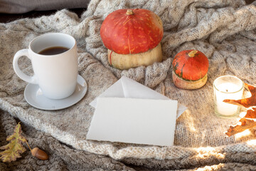 Cozy autumn breakfast scene. Blank greeting card mockup and envelope with cup of coffee or tea, candle, pumpkins.Plaid wool background.Thanksgiving, halloween concept.Natural sunlight in the morning