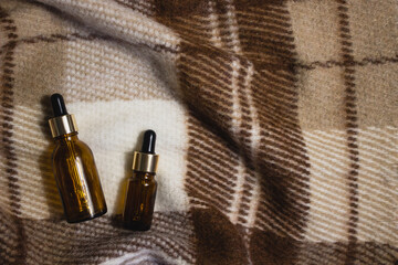 View from above. A brown plaid blanket on which there are two cosmetic brown jars with a glass pipette. Autumn.