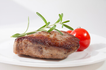 Appetizing steak well done on a white plate with tomatoes and rosemary