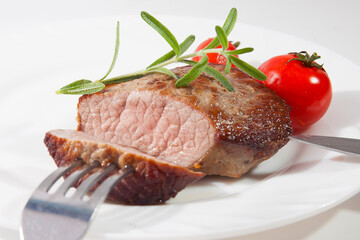 Appetizing steak well done on a white plate with tomatoes and rosemary