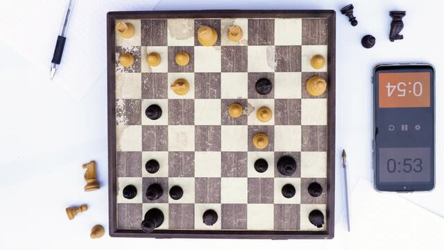 Two people playing a bullet chess game at the park. View from above on the chessboard. A smartphone is used as a clock to keep the time control.