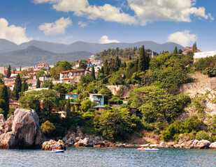 Resort settlement on the seashore. Rocks and trees, greenery and shrubs. Catamarans with tourists. Photo.