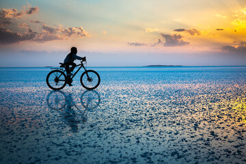 boy riding a bike over the reflection of a salt lake at sunset