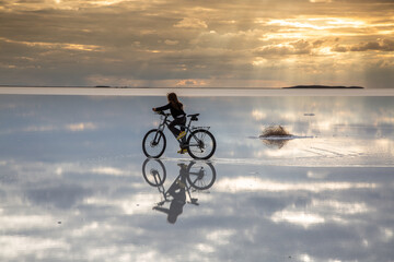 Fototapeta na wymiar boy riding a bike over the reflection of a salt lake with sunset