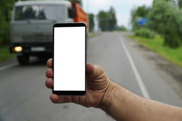 Mobile phone in a man's hand on the background of a country road with a large truck.