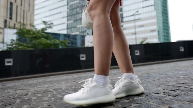 female legs in white sneakers are walking along a sloping city street. the camera goes up to the red skirt