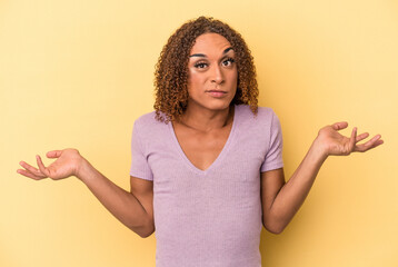 Young latin transsexual woman isolated on yellow background doubting and shrugging shoulders in...