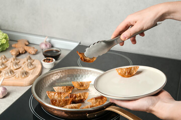 Woman serving freshly cooked delicious gyoza on plate in kitchen, closeup