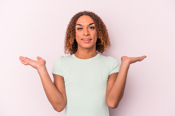 Young latin transsexual woman isolated on pink background makes scale with arms, feels happy and confident. - obrazy, fototapety, plakaty