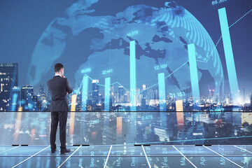 Obraz premium Back view of young european male standing on glass rooftop with forex chart, globe and night city view. Trade and stock concept. Double exposure.