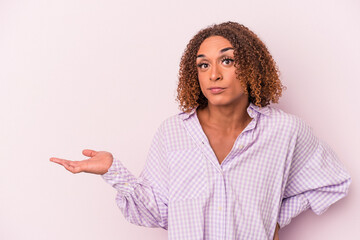 Young latin transsexual woman isolated on pink background showing a copy space on a palm and holding another hand on waist.