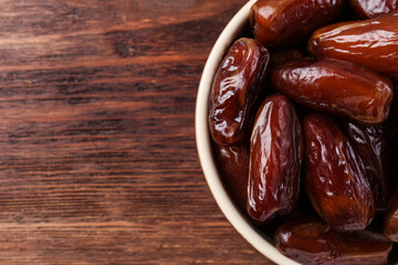 Top view of sweet dried dates in bowl on wooden background, closeup. Space for text