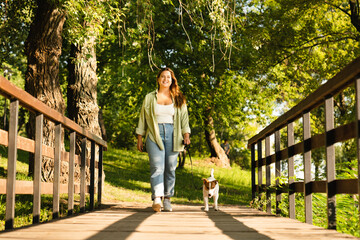 Female pet owner walking her dog in city park. Caucasian young woman playing with jack russell terrier outdoors. Pet care concept