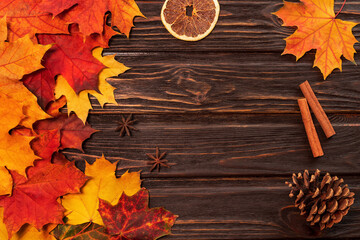 Obraz premium Autumn background with yellow and red maple leaves,cinnamon sticks, dried orange, and spruce cone. Frame of fall leaves on aged wood with copy space, top view.