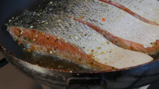 Fillet of red fish salmon salted and seasoned with pepper fried in a frying pan in the home kitchen close up view