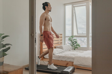Fototapeta na wymiar Asian man exercise by walking on the treadmill in his apartment.