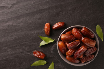 Tasty sweet dried dates and green leaves on black table, flat lay. Space for text