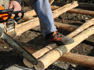 sawing off part of the logs with a chainsaw close-up, working in a village with building materials using a chainsaw, a wood sawer in the process of preparing logs for construction - obrazy, fototapety, plakaty