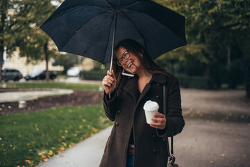 Beautiful young woman using smartphone and drinking coffee takeaway