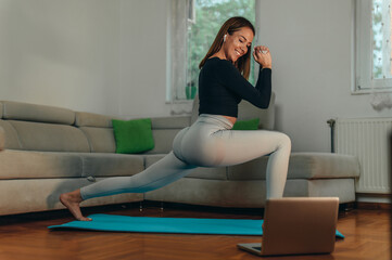 Young attractive woman training at home while using a laptop