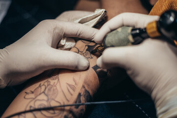 Obraz na płótnie Canvas Tattoo artist hands in a white gloves holding a machine while creating a tatto