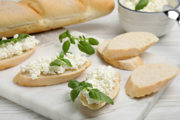 Bread with cottage cheese and basil on white wooden table, closeup