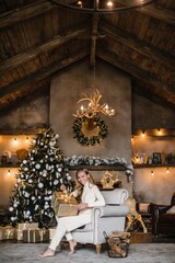 Fototapeta na wymiar young beautiful woman model with long hair in a beige suit christmas tree christmas In brown wooden houses 