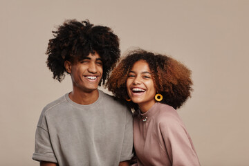 Minimal portrait of young African-American couple with natural curly hair smiling at camera against beige background, copy space