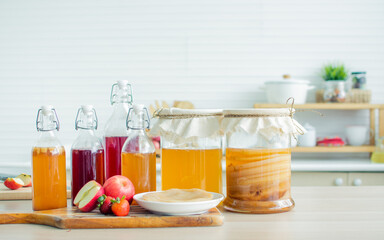 Portrait glass bottles of Kombucha healthy fermented probiotic tea drinks with ingredients red apples, strawberries, mushroom scoby on wooden table in comfortable kitchen at home. Beverange Concept.