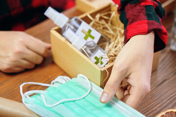 Men's hands take medical masks to put them in a gift box with antiseptics. Gift in quarantine on a wooden table. Sticker with a green cross on the sanitizers.