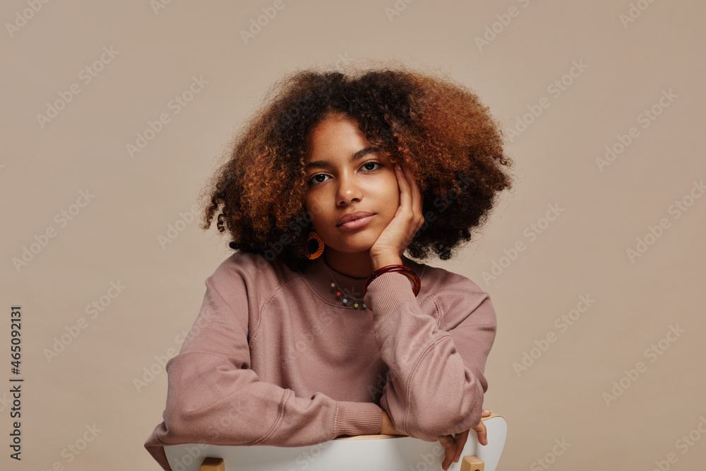 Wall mural Minimal portrait of young African-American woman with natural curly hair looking at camera in studio against beige background