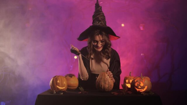 beautiful witch laughs and cuts a pumpkin for halloween