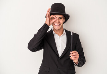 Young magician caucasian man holding a wand isolated on white background excited keeping ok gesture on eye.