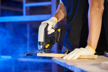 jigsaw in male hands in gloves saws a piece of wood